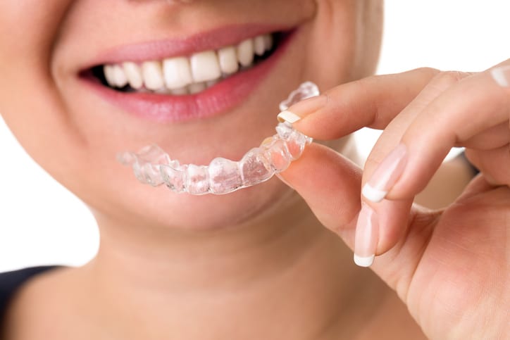 smiling female holding invisible teeth braces front of perfect smile